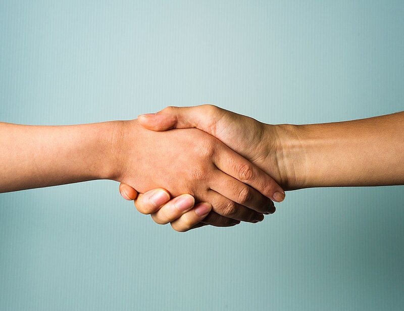 Zwei Hände schütteln sich vor einem hellen Hintergrund. Der Händedruck symbolisiert Freundschaft, Zusammenarbeit oder einen Vertrag.